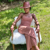 Woman in a pink dress and burgundy hat sitting on a white furry chair outdoors.