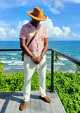 Man wearing a tan tear drop hat and patterned shirt standing on a deck with ocean view